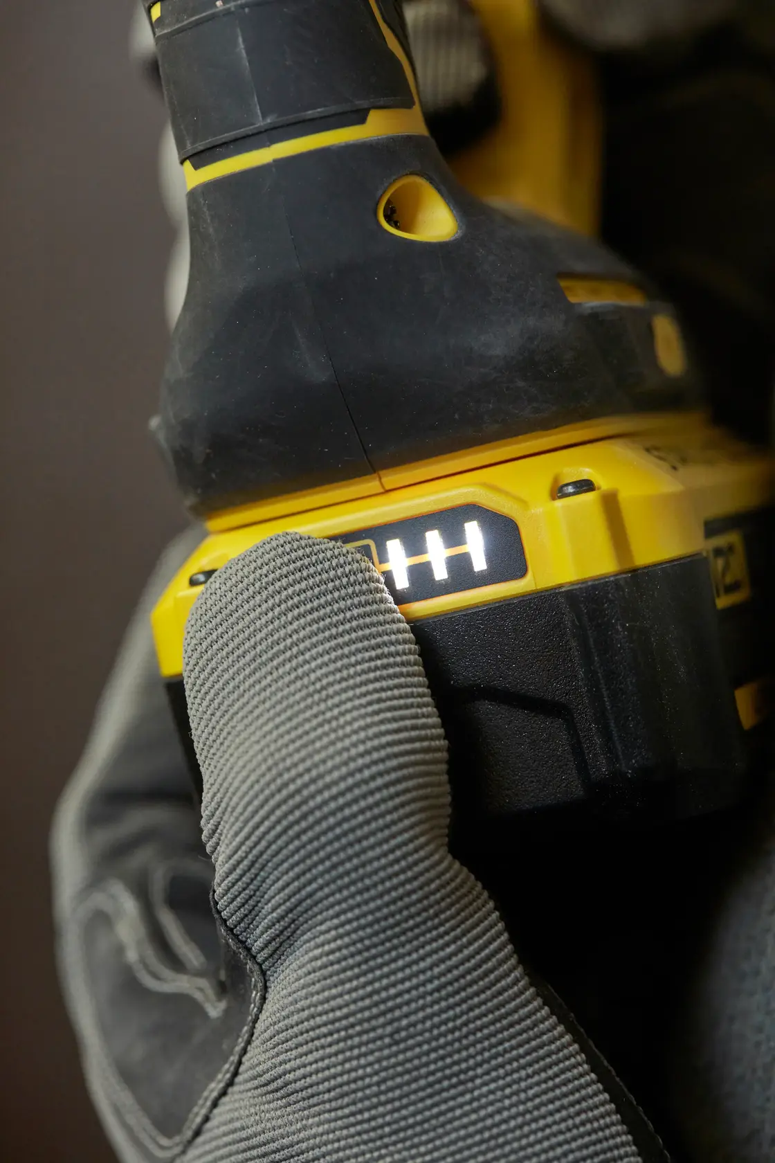 STANLEY SBH900M2K-B3 batería de herramienta eléctrica en primer plano, guante presionando indicador LED, ángulo lateral.