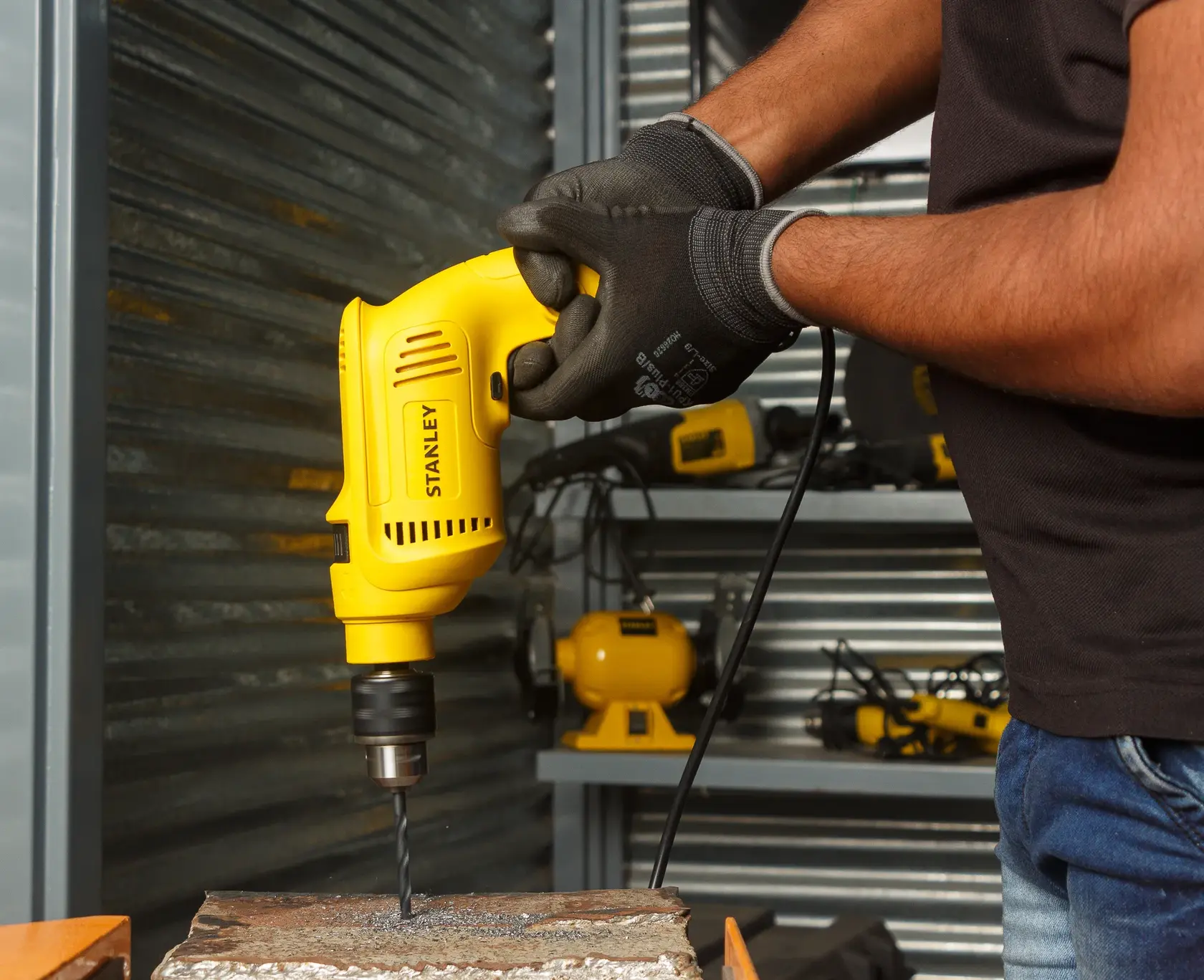 Taladro con cable amarillo Stanley SDH600KP perforando metal, ángulo lateral en taller.
