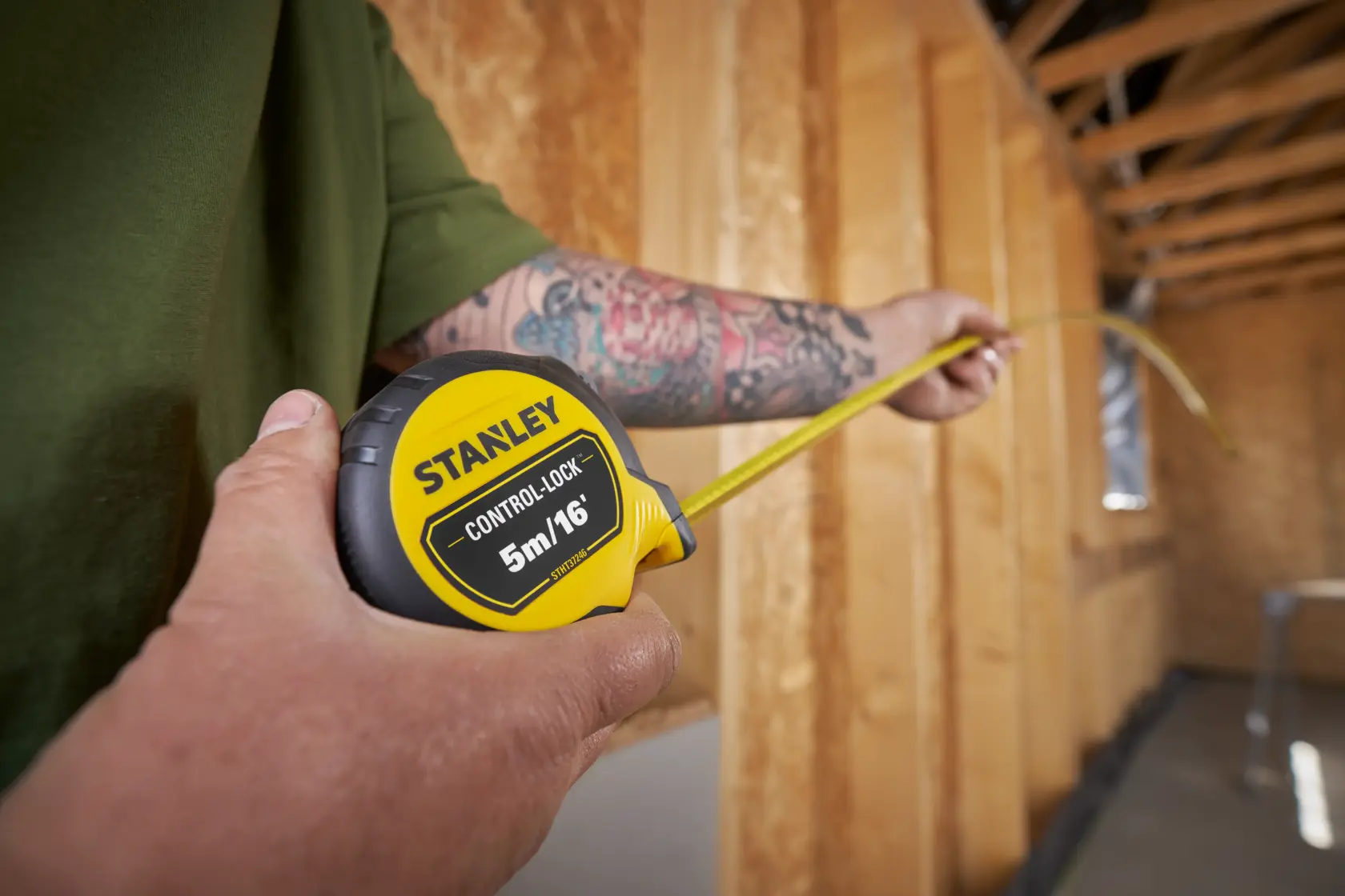 Stanley STHT37246-0 cinta métrica sostenida en la mano, midiendo distancia en habitación sin terminar.